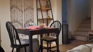 Un comedor con mesa, sillas e iluminación colgante. Se observa una escalera al fondo.