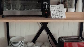 A kitchen with a black toaster oven, a red toaster, and a note on the shelf.