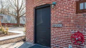 A brick building with a black door, a fire hose reel, and a number '2009' on the wall. - Barber Street Flats: #202 (Knoxville)