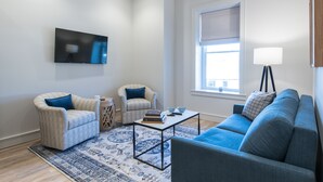 A living room with a flat-screen TV, two armchairs, a sofa, a coffee table, and a patterned rug. - Barber Street Flats: #202 (Knoxville)