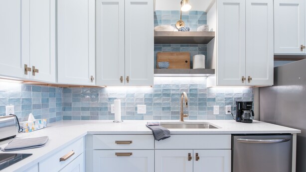 A modern kitchen with white cabinets, a stainless steel refrigerator, and a blue-tiled backsplash. - Barber Street Flats: #202 (Knoxville)