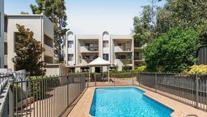 A modern building with a swimming pool, surrounded by a metal fence, and featuring balconies and greenery. - Leafy central stylish apartment in great location. (South Perth)