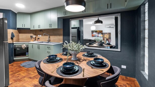A modern kitchen with light green cabinets, a central island, and a dining area with a round table set for four. - Leafy central stylish apartment in great location. (South Perth)