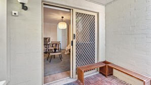 A room with a sliding glass door leading to a balcony with a wooden bench. - Leafy central stylish apartment in great location. (South Perth)