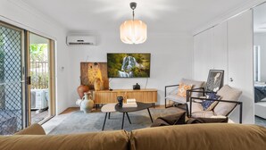 A modern living room with a sofa, a coffee table, and a TV mounted on the wall. - Leafy central stylish apartment in great location. (South Perth)