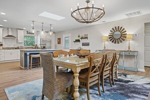Une cuisine moderne avec des meubles blancs, un îlot central et un coin repas comprenant une table à plateau en verre et des chaises en bois.