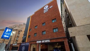 Un bâtiment moderne en briques, sur lequel on peut voir une enseigne indiquant l’hôtel Brown-Dot. Un panneau de signalisation indique la présence d’un parking sur la gauche.