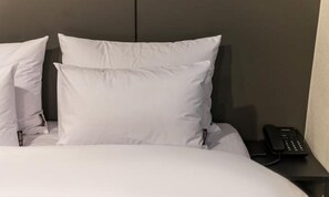 A hotel room with a bed, white pillows, a black telephone, and a dark headboard.