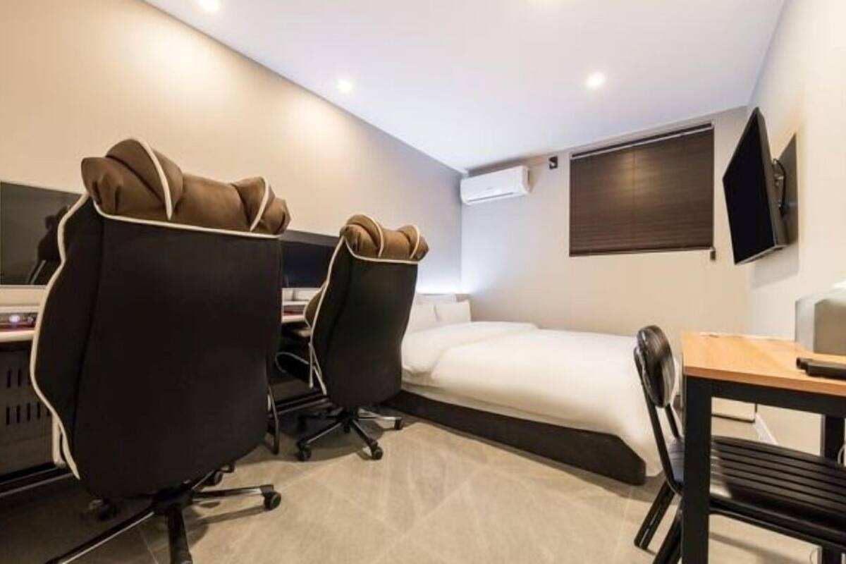 Een moderne hotelkamer met een bed, twee bureaustoelen, een bureau en een kleine tafel.