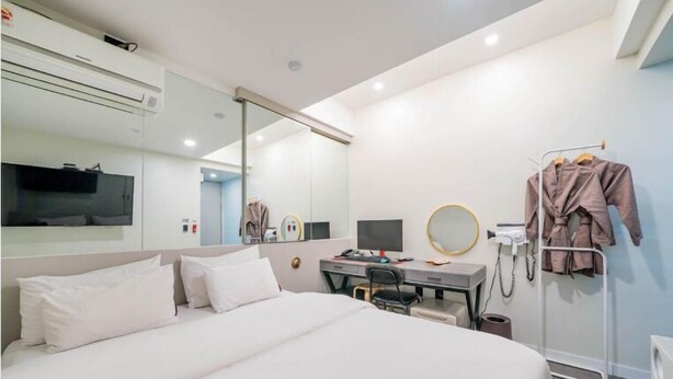 Une chambre d’hôtel comprenant un lit, un bureau avec un ordinateur, un miroir et un porte-peignoir.