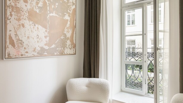 A modern living room with a large abstract painting, a white armchair, a round wooden side table, and a view of a balcony with a geometric railing. - Piękna Chic Apartment (Warszawa)