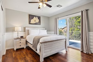A bedroom with a bed, a nightstand, a ceiling fan, a window with curtains, and a view of greenery outside.