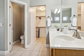 A bathroom with a toilet, a sink, a mirror, and a shower area. - Vacay In The Valley - Entertainers Backyard! (Gilbert)