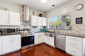 A modern kitchen with white cabinets, stainless steel appliances, a window with a view, and a clock on the wall.