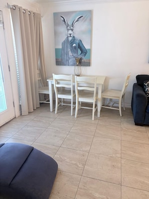 A room with a dining table, chairs, a painting, a potted plant, and a sofa.