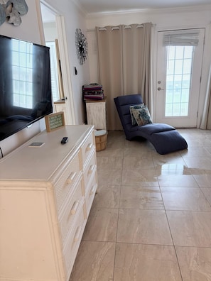 Una sala de estar con televisor, sofá, mueble y puerta con cortinas.