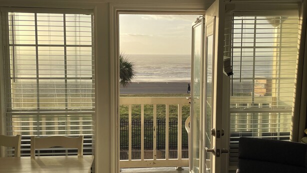 Une chambre avec vue sur l’océan grâce à de grandes fenêtres, un balcon avec une balustrade et une table avec des chaises.