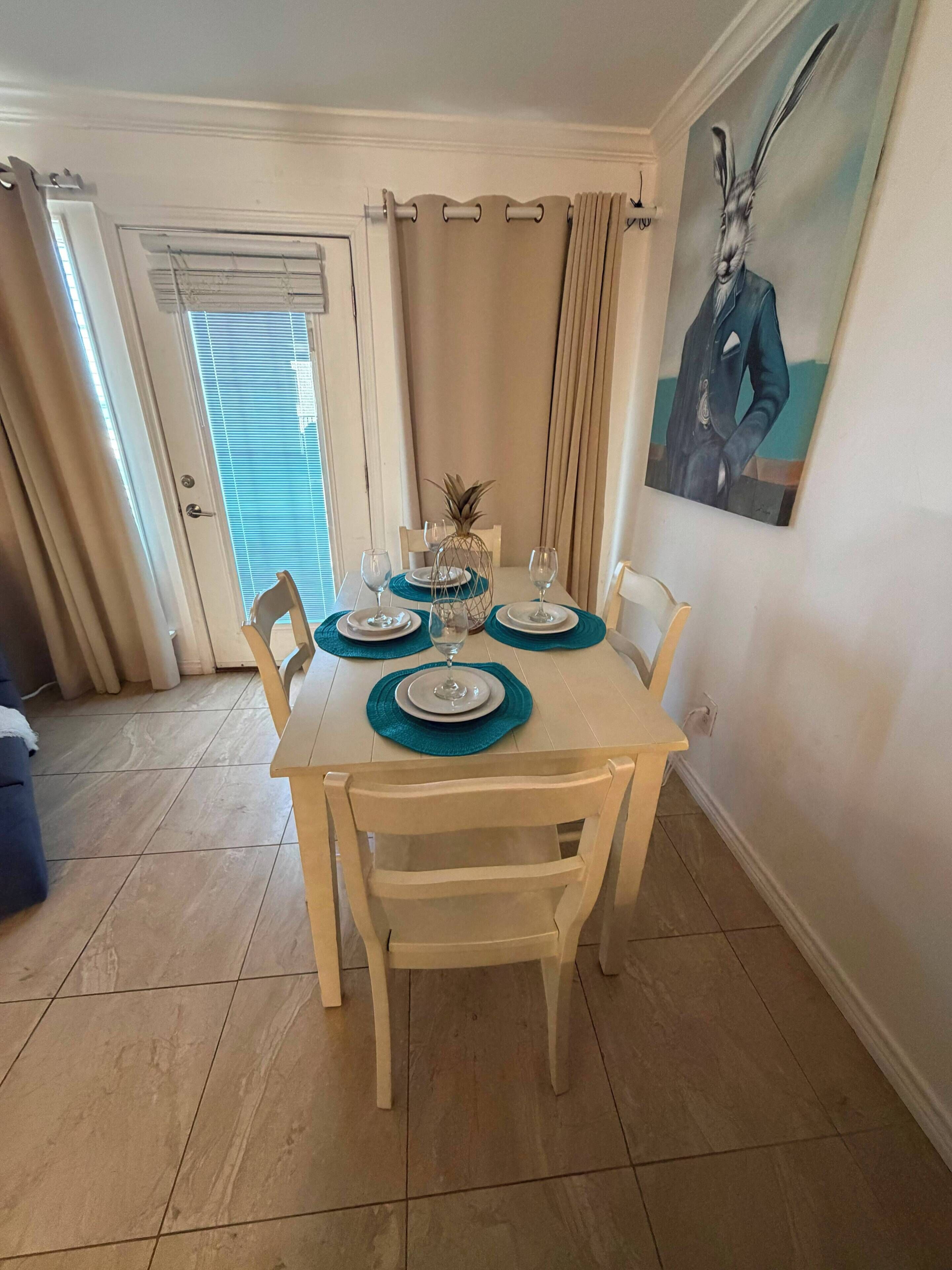 A dining area with a table set for four, chairs, a pineapple centerpiece, and a painting on the wall.