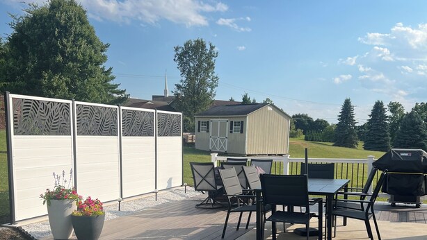 Un patio al aire libre con una mesa y sillas, una parrilla, y un área cercada con paneles decorativos.