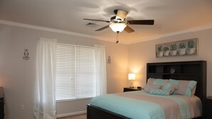 Un dormitorio con cama, ventilador de techo, ventana con persianas, mesita de noche y lámpara de pared.