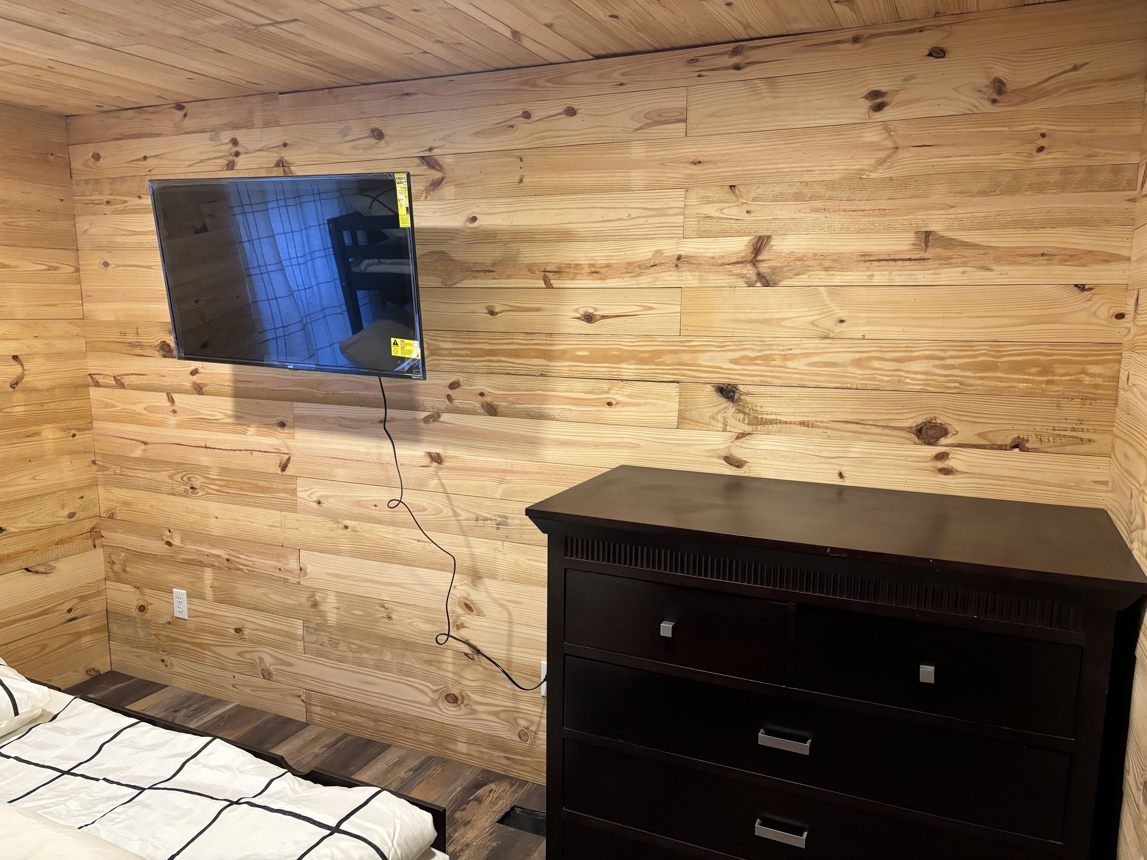 A wooden-paneled room with a bed, a dresser, and a mounted television.