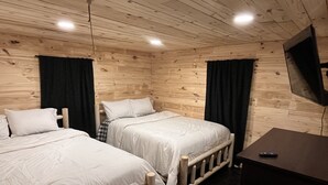 Una habitación tipo cabaña de madera con dos camas, un escritorio y un televisor montado en la pared.