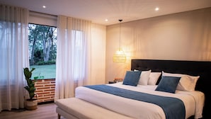 A modern bedroom with a large bed, a bench, a potted plant, and a view of greenery outside. - Monarch Campestre (El Carmen de Viboral)