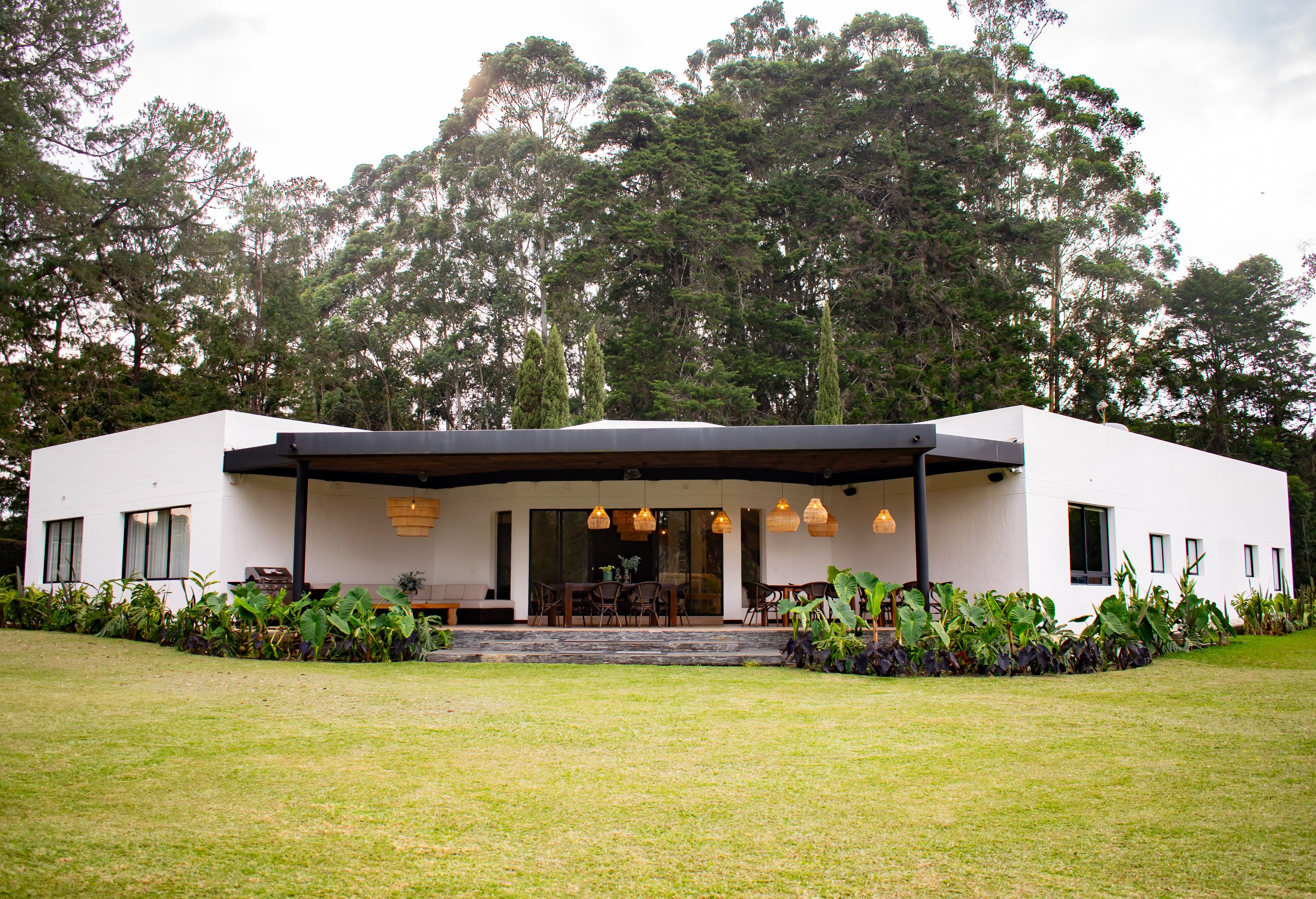 A modern house with a covered patio, a dining area, and a large lawn.