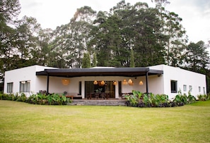 A modern house with a covered patio, a dining area, and a large lawn.