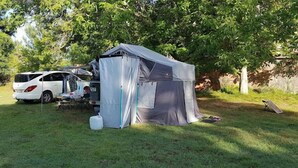 Un campamento con una tienda de campaña, un automóvil y equipo de acampada en un área con césped y árboles.