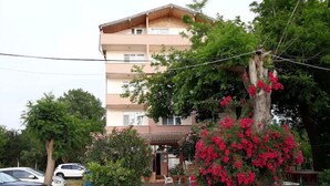Un edificio de varios pisos con balcón, rodeado de vegetación y automóviles estacionados.