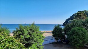A beach with a clear view of the sea, surrounded by greenery and a rocky cliff. - PINAR OTEL (Amasra)