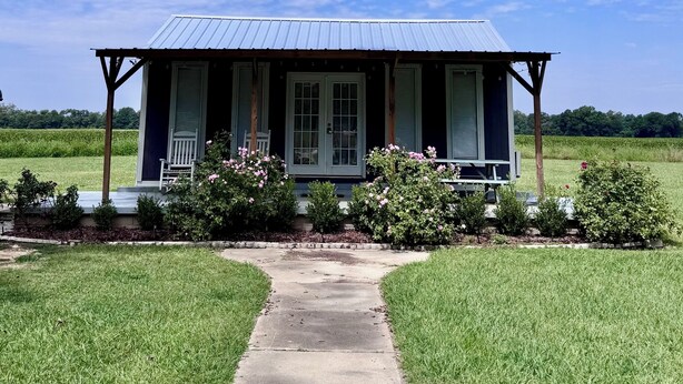 A house with a porch, a pathway leading to it, and a grassy field in the background. - James' Cabin (Gilbert)
