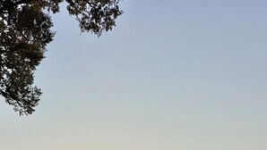 A rural setting with a red pickup truck parked under a covered area, a small building with a porch, and a clear sky during sunset. - James' Cabin (Gilbert)