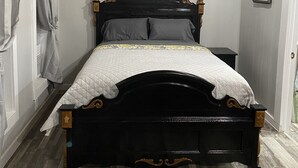 A bed with a wooden headboard, a white quilted bedspread, and a nightstand with a lamp. - James' Cabin (Gilbert)