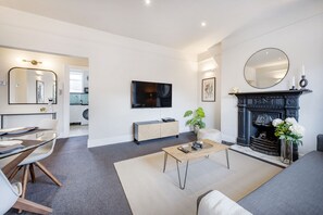 A modern living room with a sofa, coffee table, and fireplace. There is a television mounted on the wall and a mirror above the fireplace. - NEW! 2Bed/3Beds/1Bath/Cov Gd Piazza/1 min subway (Greater London)