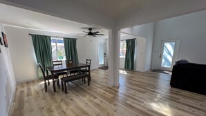 A spacious living area with a dining table, chairs, a ceiling fan, and a black couch. - Bayside Cove Retreat: Your Coastal Escape (Shalimar)