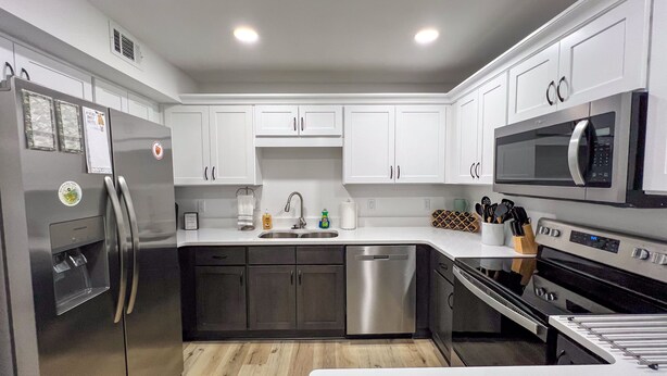A modern kitchen with white cabinets, stainless steel appliances, and a wooden floor. - Bayside Cove Retreat: Your Coastal Escape (Shalimar)
