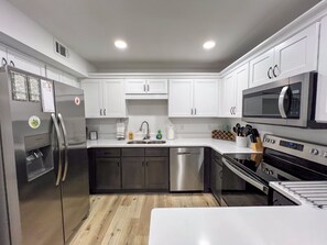 Une cuisine moderne avec des armoires blanches, des appareils en acier inoxydable et un plancher en bois.