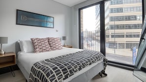 A modern hotel room with a large bed, a view of the city through a large window, and a framed artwork on the wall. - Exceptional Aldgate/Whitechapel 2BR w/ Garden, nr Station, by Blueground (London)