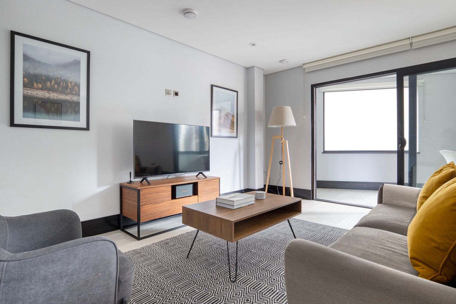 Un soggiorno moderno con una TV a schermo piatto su un supporto in legno, una lampada da terra, un divano e un tavolino da caffè con libri.