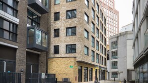 A multi-story building with a brick facade, large windows, and a ground-level entrance with a sign. - Exceptional Aldgate/Whitechapel 2BR w/ Garden, nr Station, by Blueground (London)