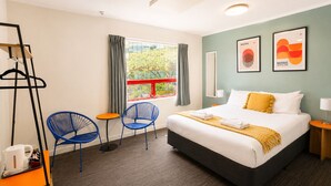 A hotel room with a bed, two chairs, a table, a coat rack, and artwork on the wall. - United Auckland (Auckland)