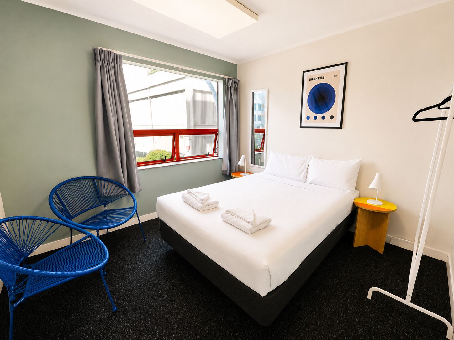 A hotel room with a bed, a chair, a window, and a wall-mounted picture.