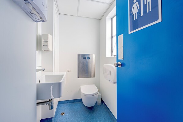 Une petite salle de bain propre, équipée d’un lavabo, de toilettes et d’un sèche-mains.