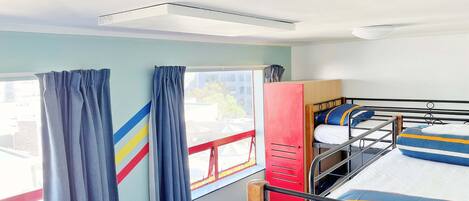 A dormitory room with bunk beds, a red wardrobe, and a window with curtains.
