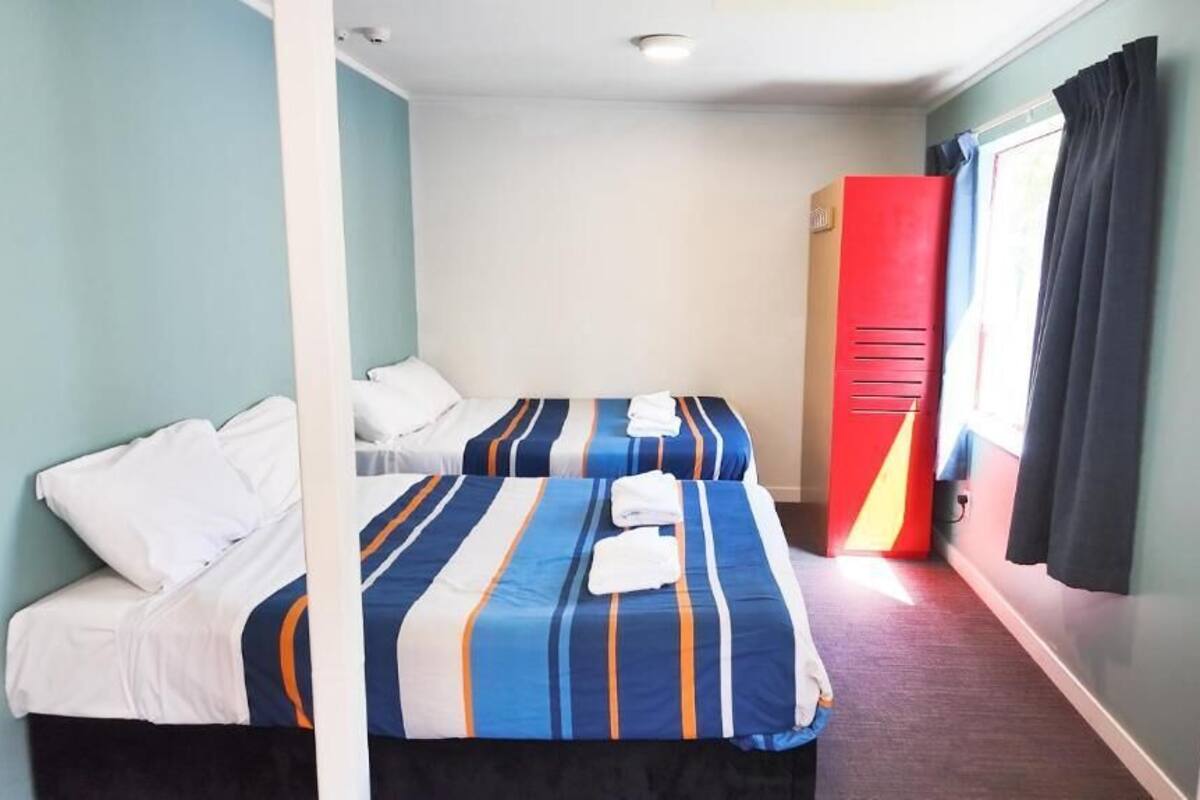 A room with two beds, a red wardrobe, and a window with curtains.
