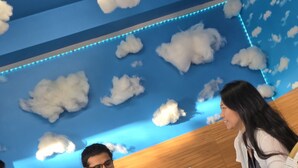 A meeting room with a blue ceiling decorated with cloud patterns and LED lights, a white table with a laptop, a potted plant, and a small sign. - United Auckland (Auckland)