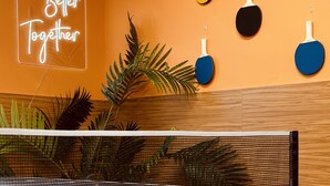 A ping pong table with paddles in a room with orange walls and a neon sign that reads "Better Together". - United Auckland (Auckland)