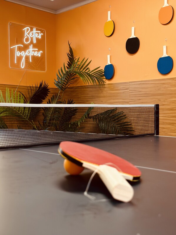A ping pong table with paddles in a room with orange walls and a neon sign that reads "Better Together". - United Auckland (Auckland)